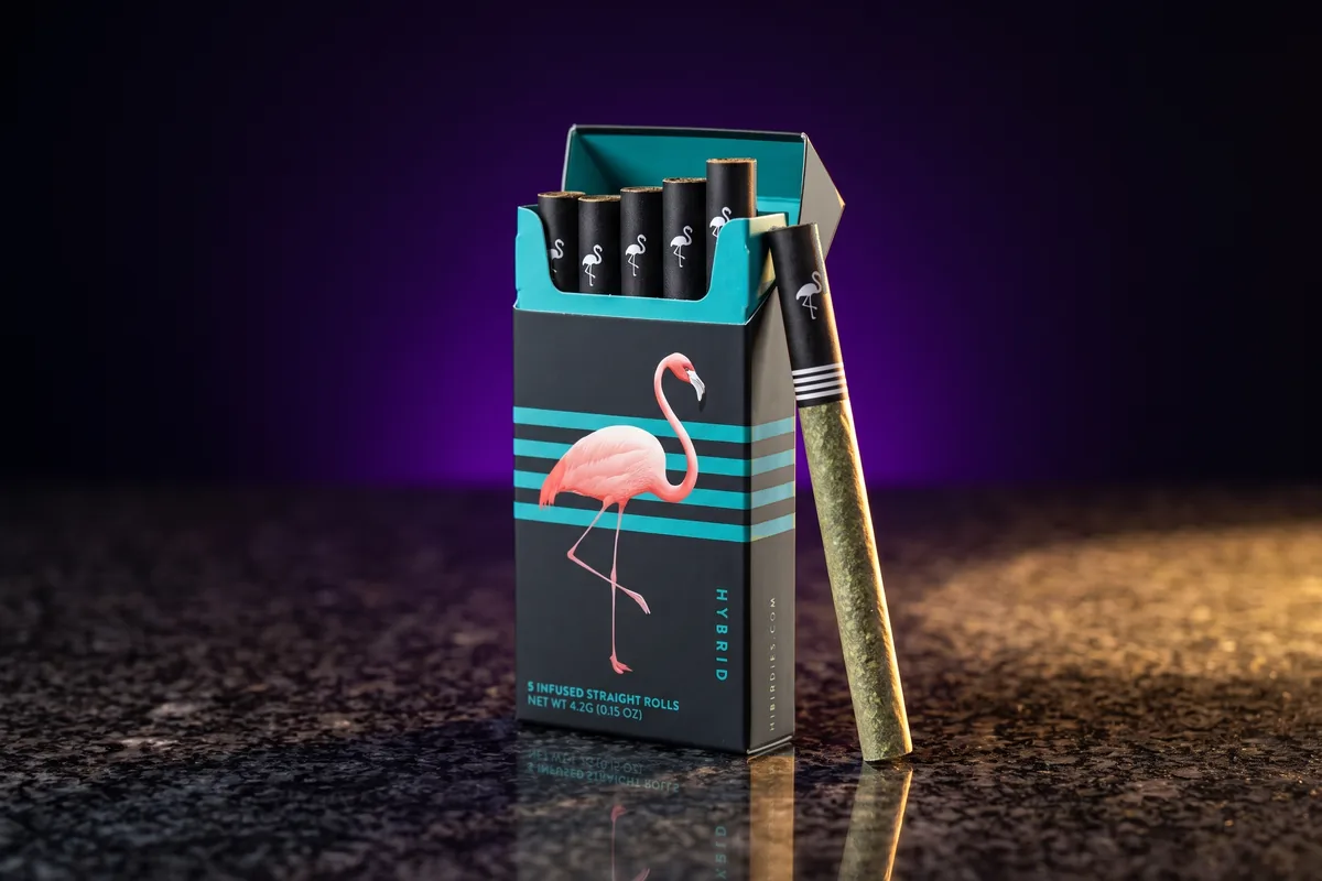An open black Birdies Ultra Infused 5-pack, Hybrid, with teal stripes and a pink flamingo, and a black pre-roll leaning on its side, on dark granite.