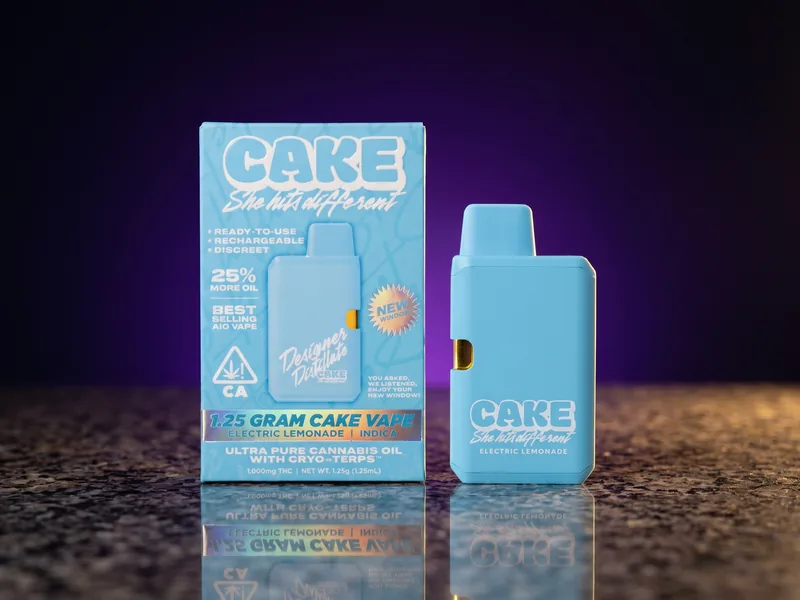 A sky-blue CAKE 1.25g all-in-one vape box in Electric Lemonade, Indica, with the matching sky-blue CAKE device beside it, on dark granite.