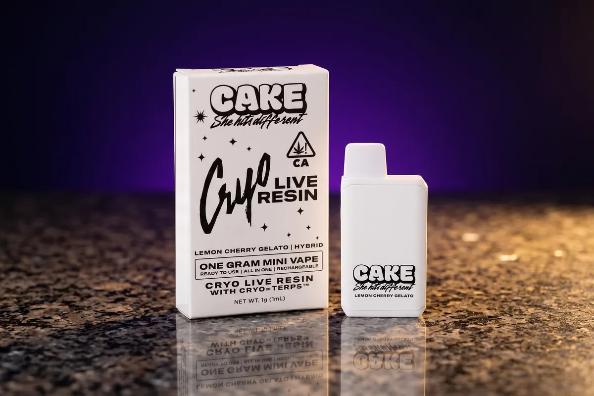 A white CAKE Cryo Live Resin box in Lemon Cherry Gelato, a one gram mini vape, with the matching white CAKE device beside it on dark granite.