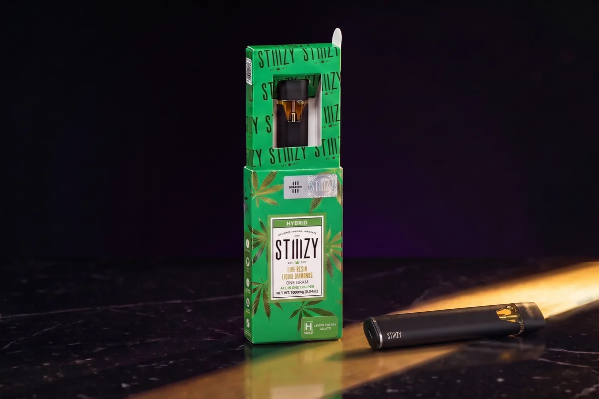 A STIIIZY Live Resin Liquid Diamonds all-in-one box in Lemon Cherry Gelato, with one slim black STIIIZY all-in-one vape in front of it.