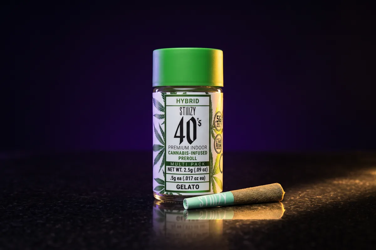 A STIIIZY 40's Gelato infused pre-roll jar with a green cap, and one pre-roll with a mint-green STIIIZY tip lying in front of it.