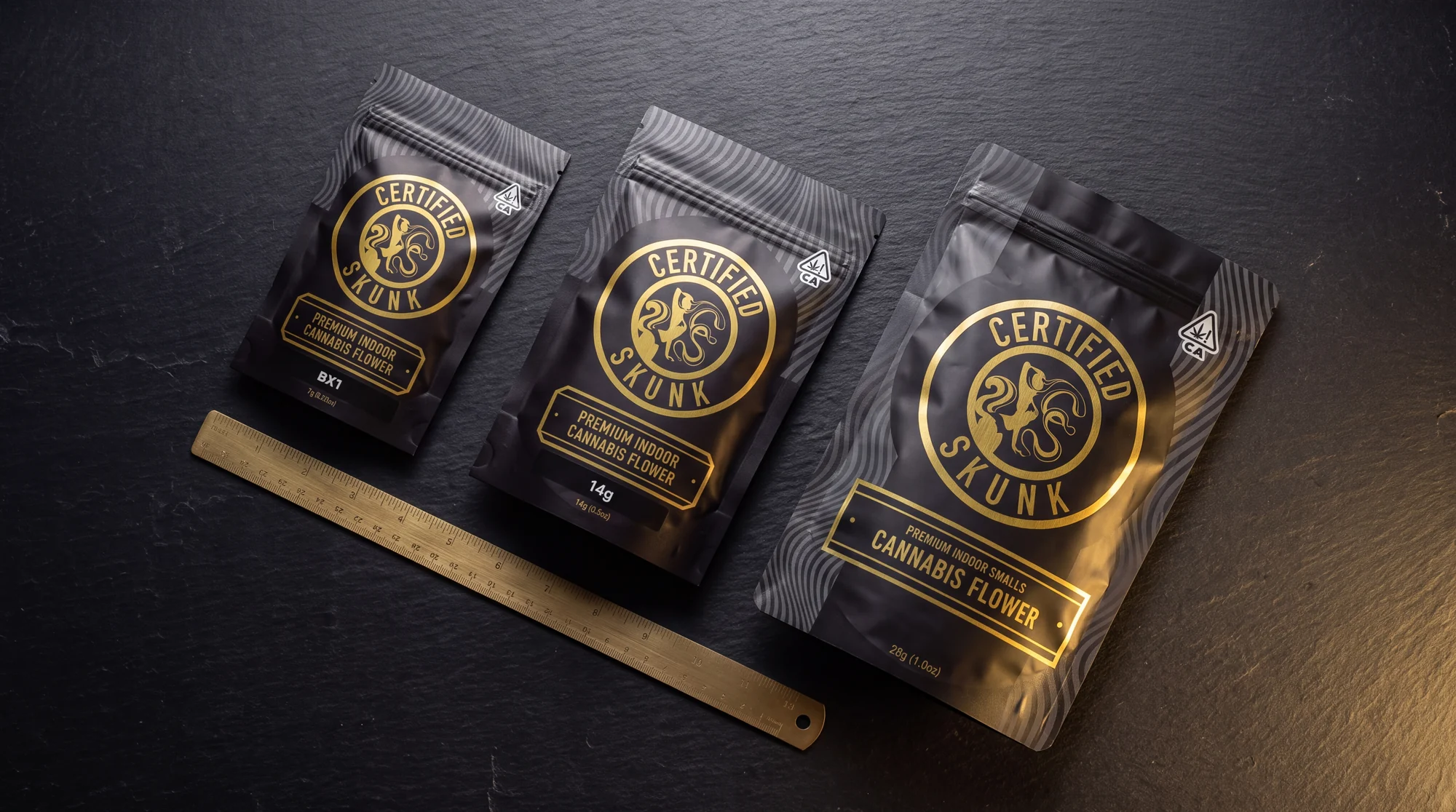 Certified Skunk pouches in 7g, 14g and 28g laid flat beside a brass rule