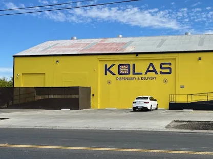 The yellow KOLAS Blumenfeld building from across the street, with the KOLAS Dispensary and Delivery sign